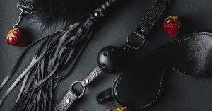 A stylish flat lay of leather BDSM accessories with fresh strawberries on a dark background.